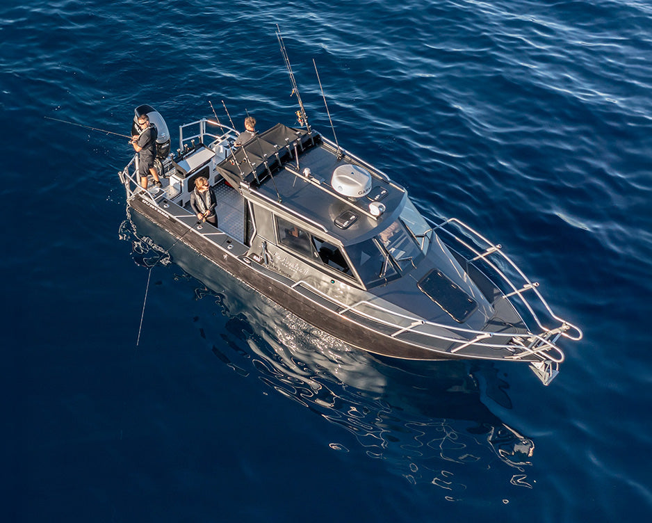 A dark gray fishing boat with people on board, view from an aerial perspective to show the boat hatch.